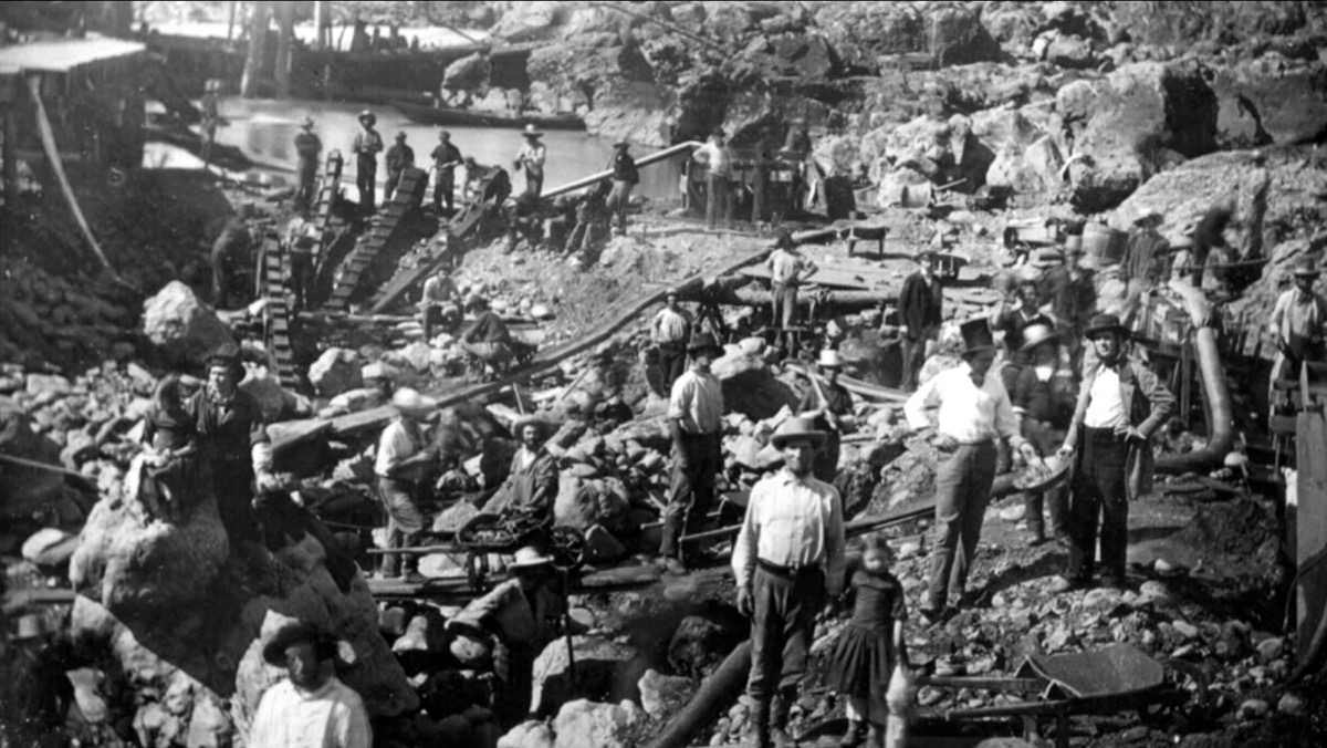 Gold Rush mining operation on the American River near Sacramento, circa 1852 — dozens of miners crowded onto one riverbank with picks and sluicing equipment