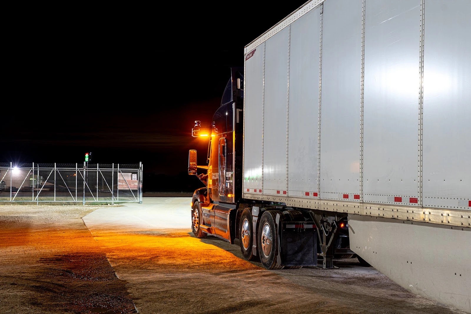 An Aurora driverless truck stopped at night with its amber cab-mounted warning beacon lit on the cab roof