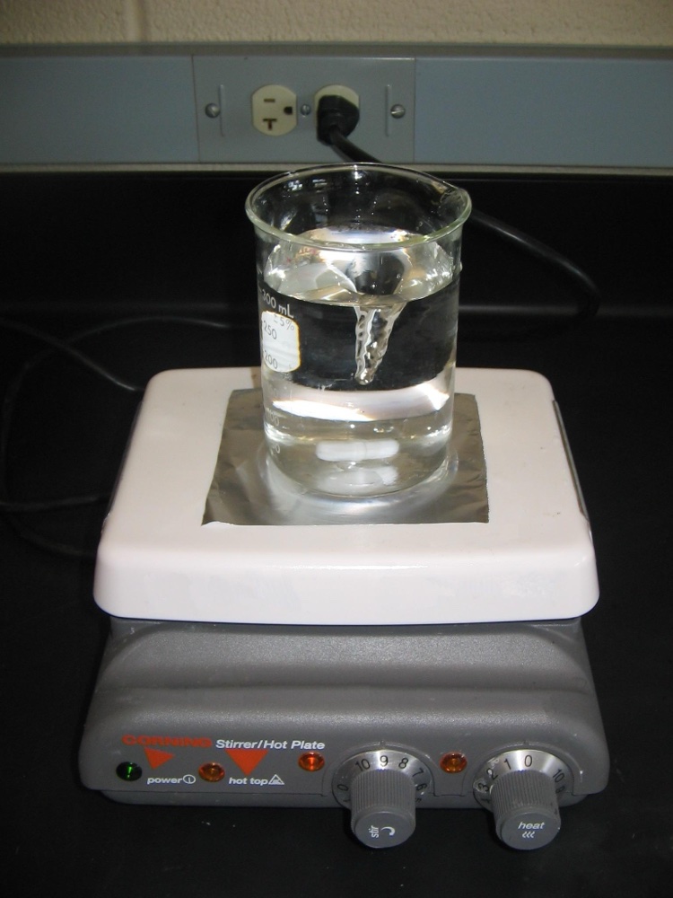 A laboratory magnetic stirrer mixing a solution in a beaker — the stir-speed dial that controls stirring intensity is visible