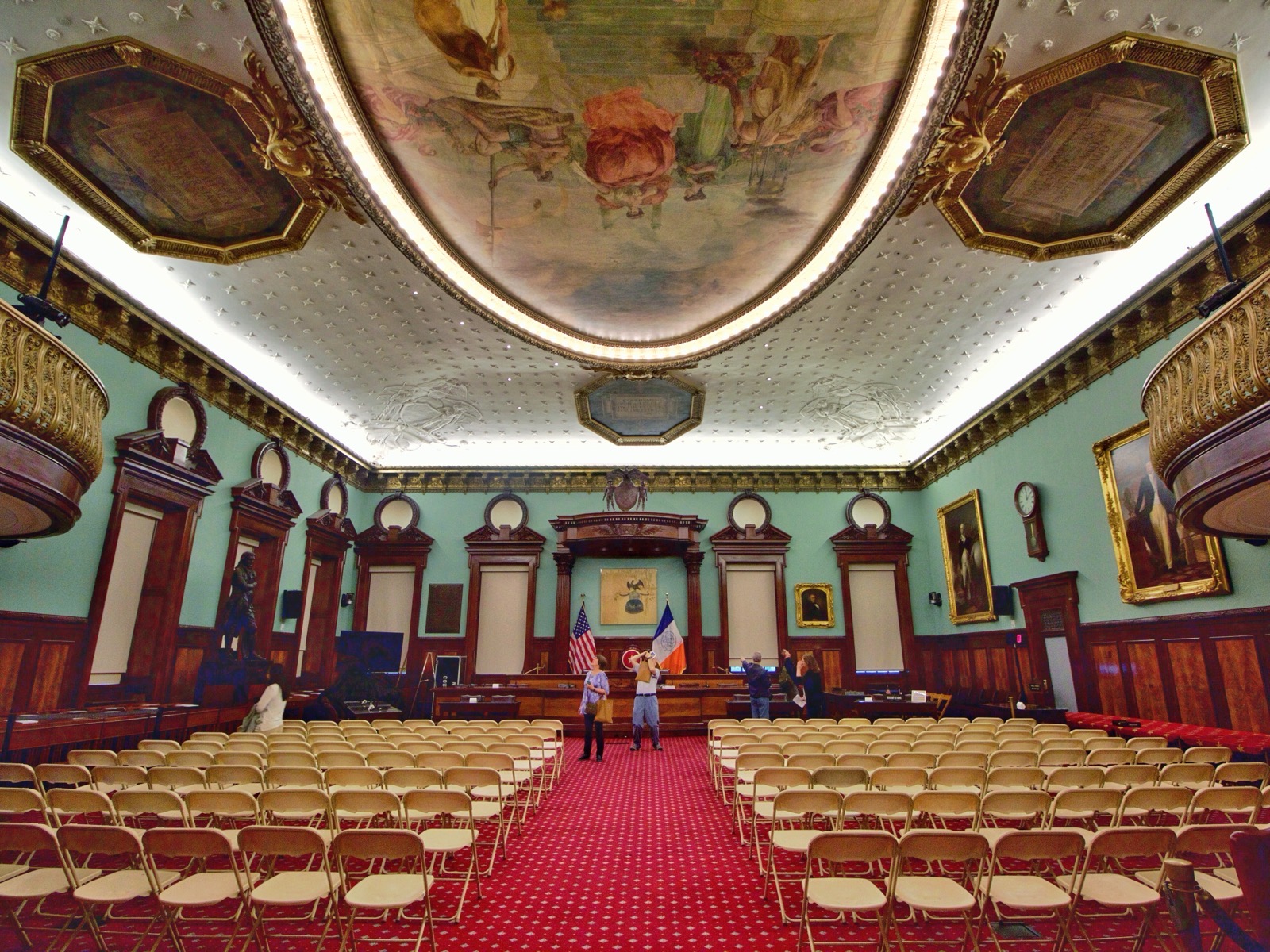 Interior of the New York City Council chamber at City Hall, with the dais, American flag, and New York City flag