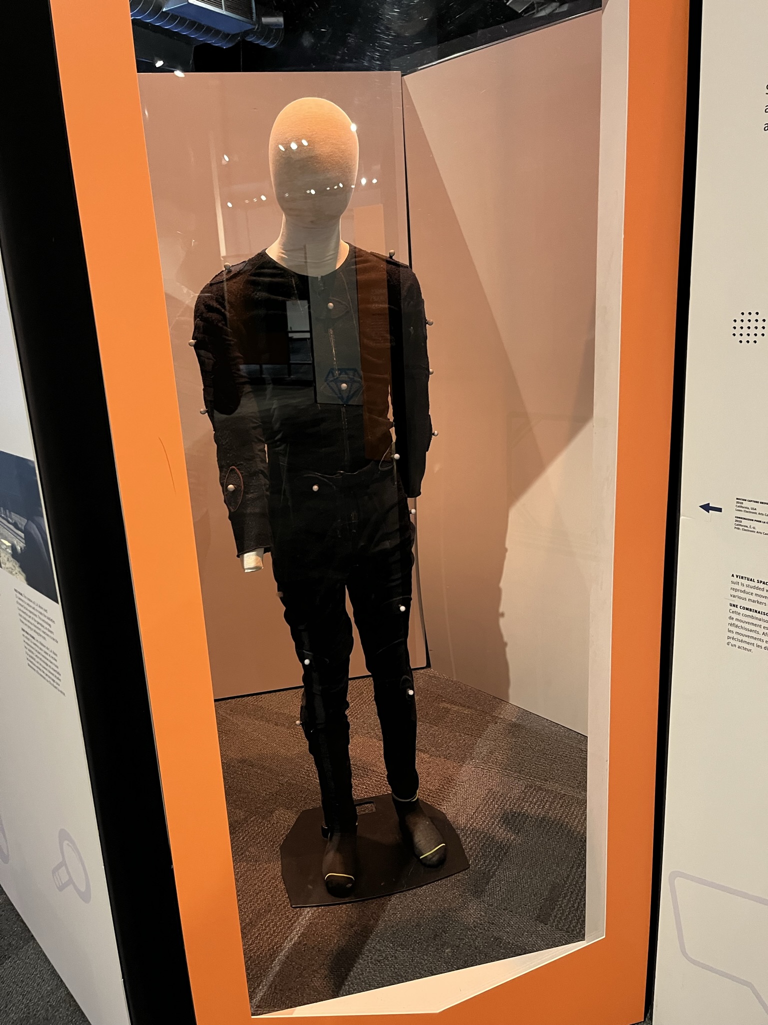 A motion capture suit with reflective markers attached across the full body, displayed on a mannequin