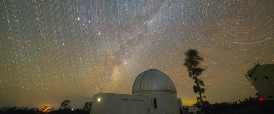 Long-exposure night photo of star trails circling above a KMTNet observatory dome, symbolizing a decade of accumulated observing records