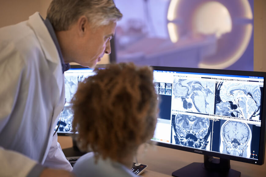 영상의학과 의사가 동료와 함께 MRI 판독 화면을 확인하는 모습 — 민감도·특이도 같은 잣대로 먼저 검증받은 진단 AI 채널을 보여 준다