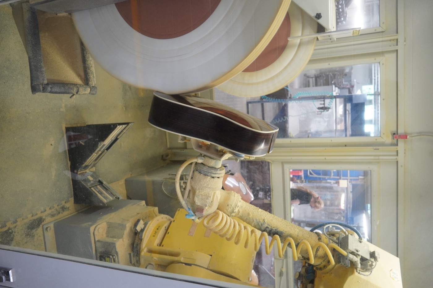 Industrial robot arm holding a guitar body against a buffing wheel