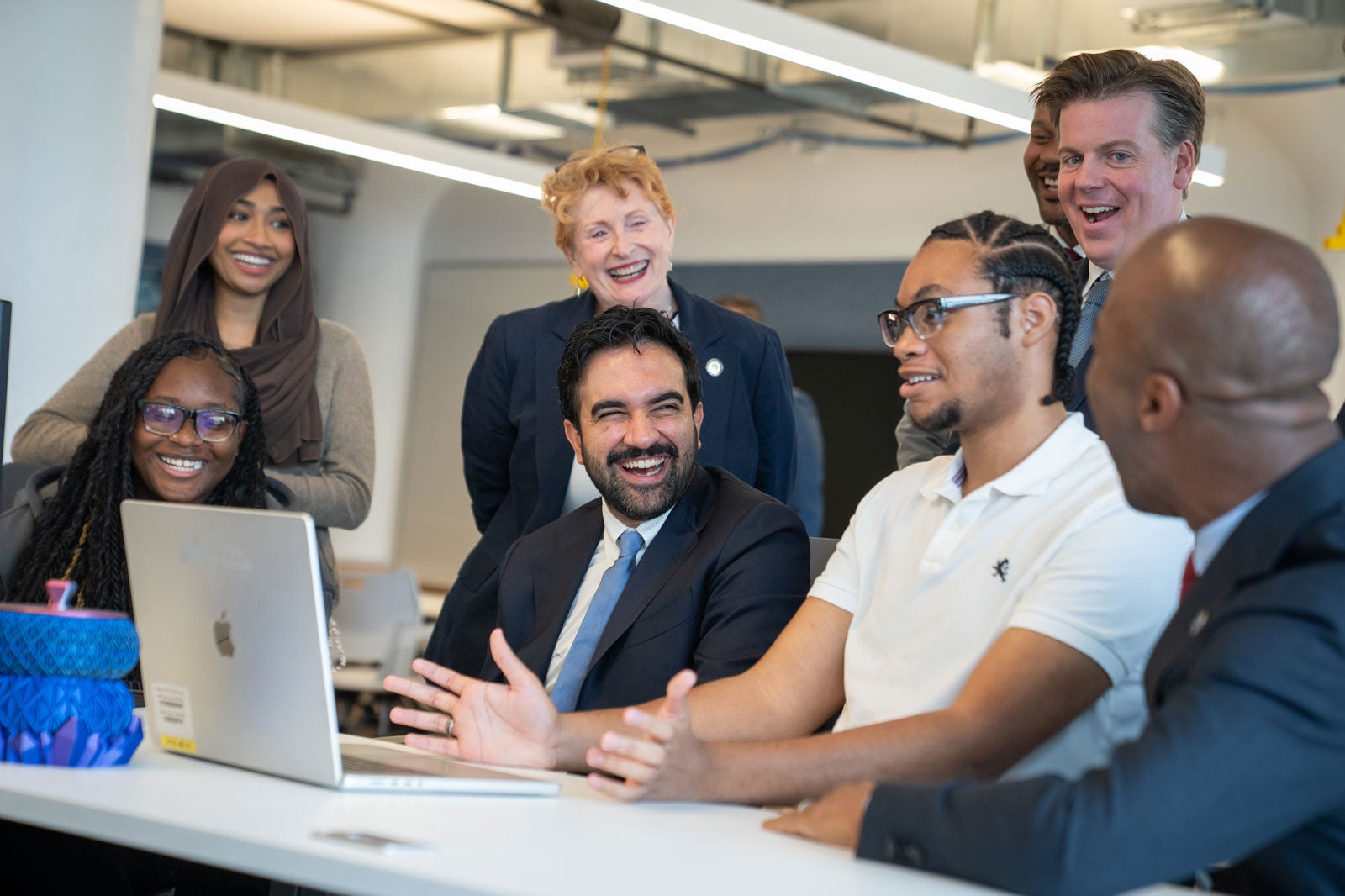 Mayor Mamdani looking at a laptop with students at the Brooklyn STEAM Center during the policy announcement