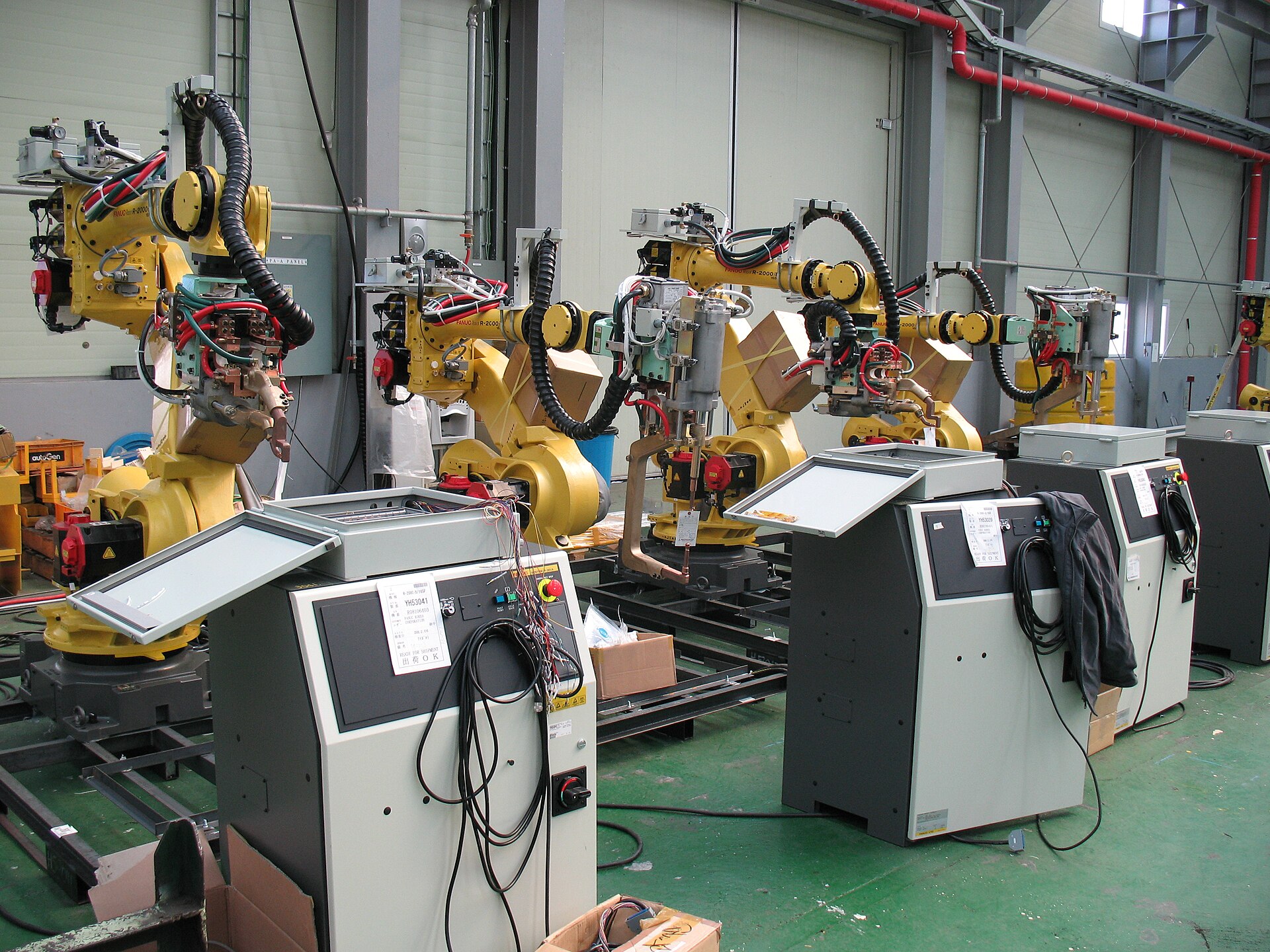 A FANUC industrial robot arm at work on a factory floor — joint backlash and friction shape action accuracy